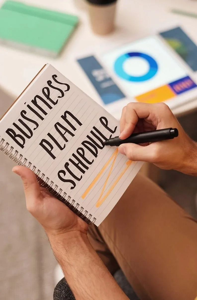 ノートに「Business Plan Schedule」と書く手元